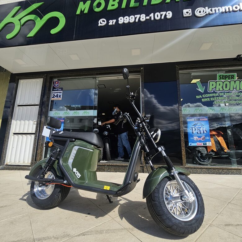 Scooter elétrica verde militar estilo chopper em frente à loja da KM
